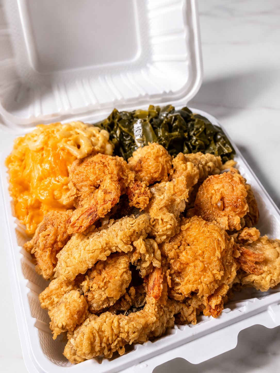 Fried shrimp, macaroni and cheese, and collard greens in a takeout container.