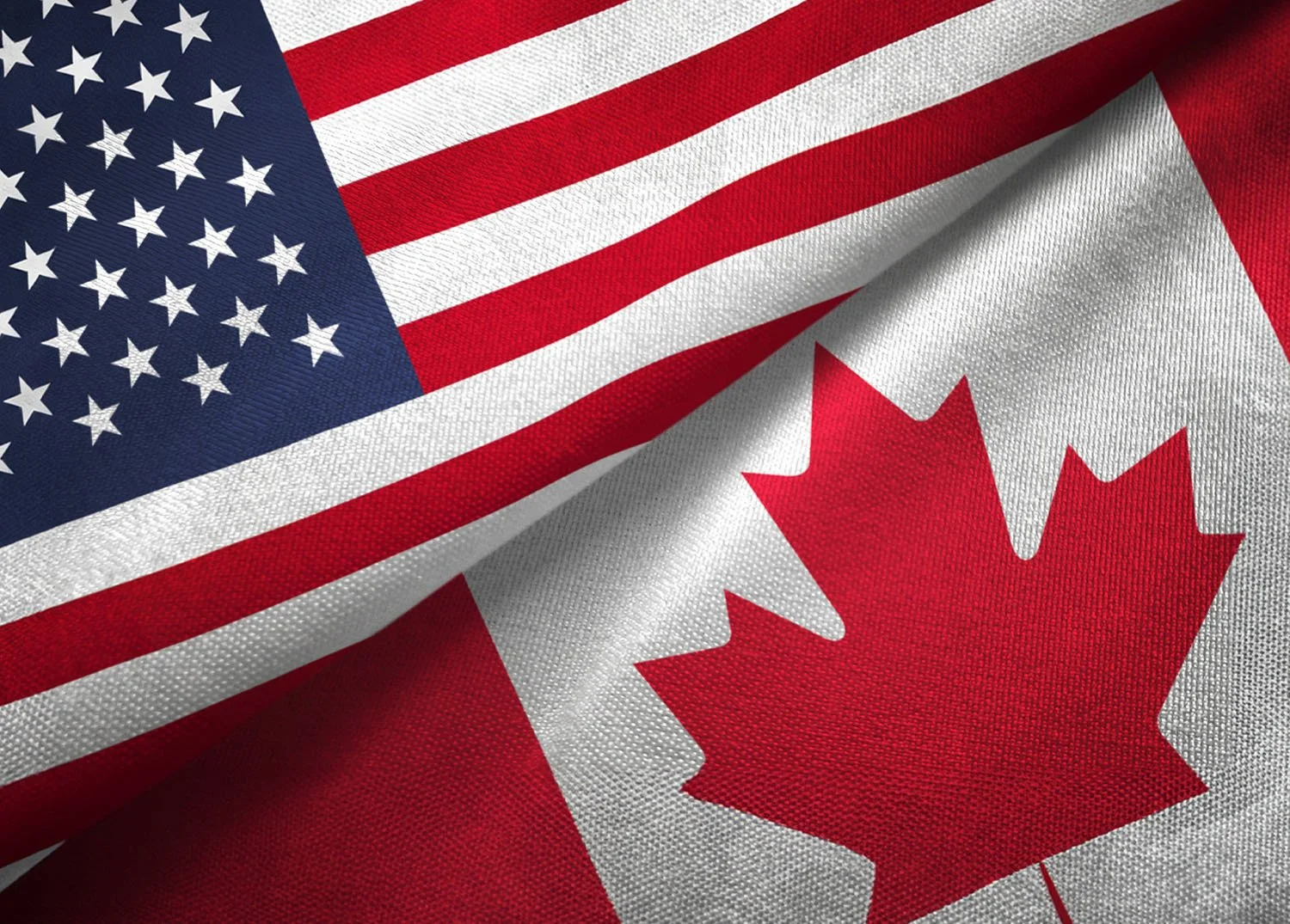 A close-up of the United States flag overlapping a close-up of the Canadian flag.