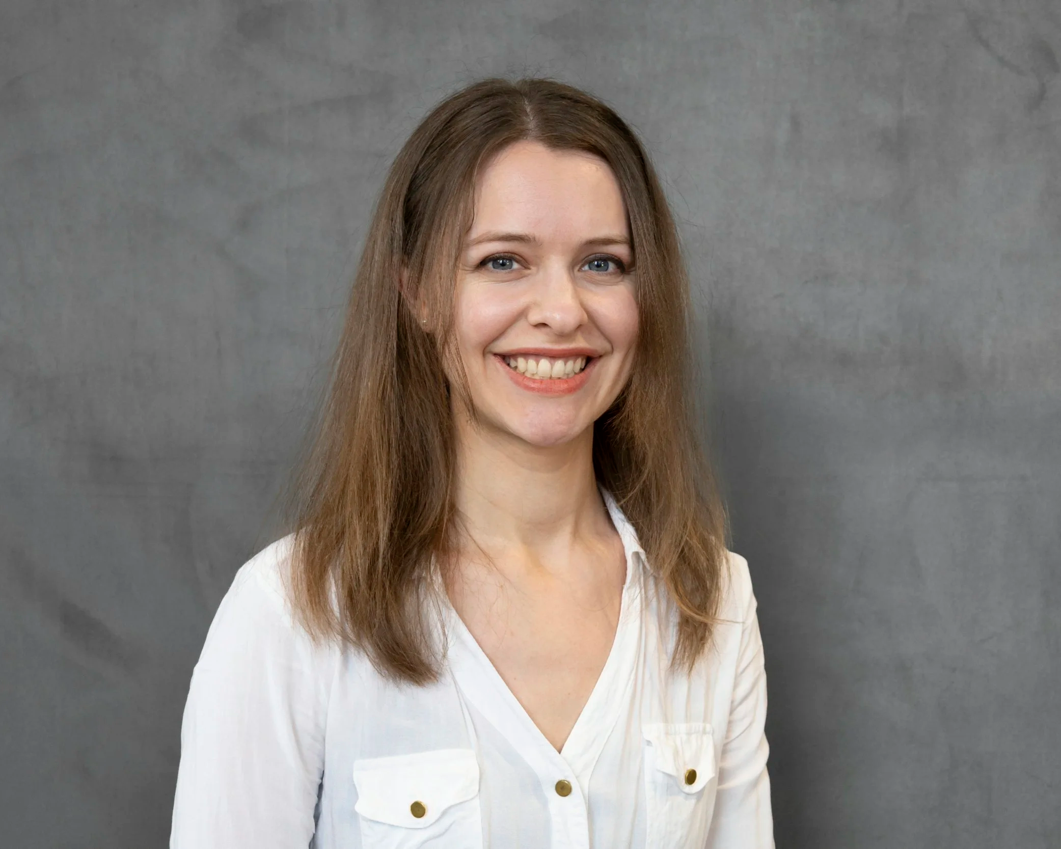 Smiling female legal professional with straight brown hair wearing a white button-up shirt, posed against a gray studio background.