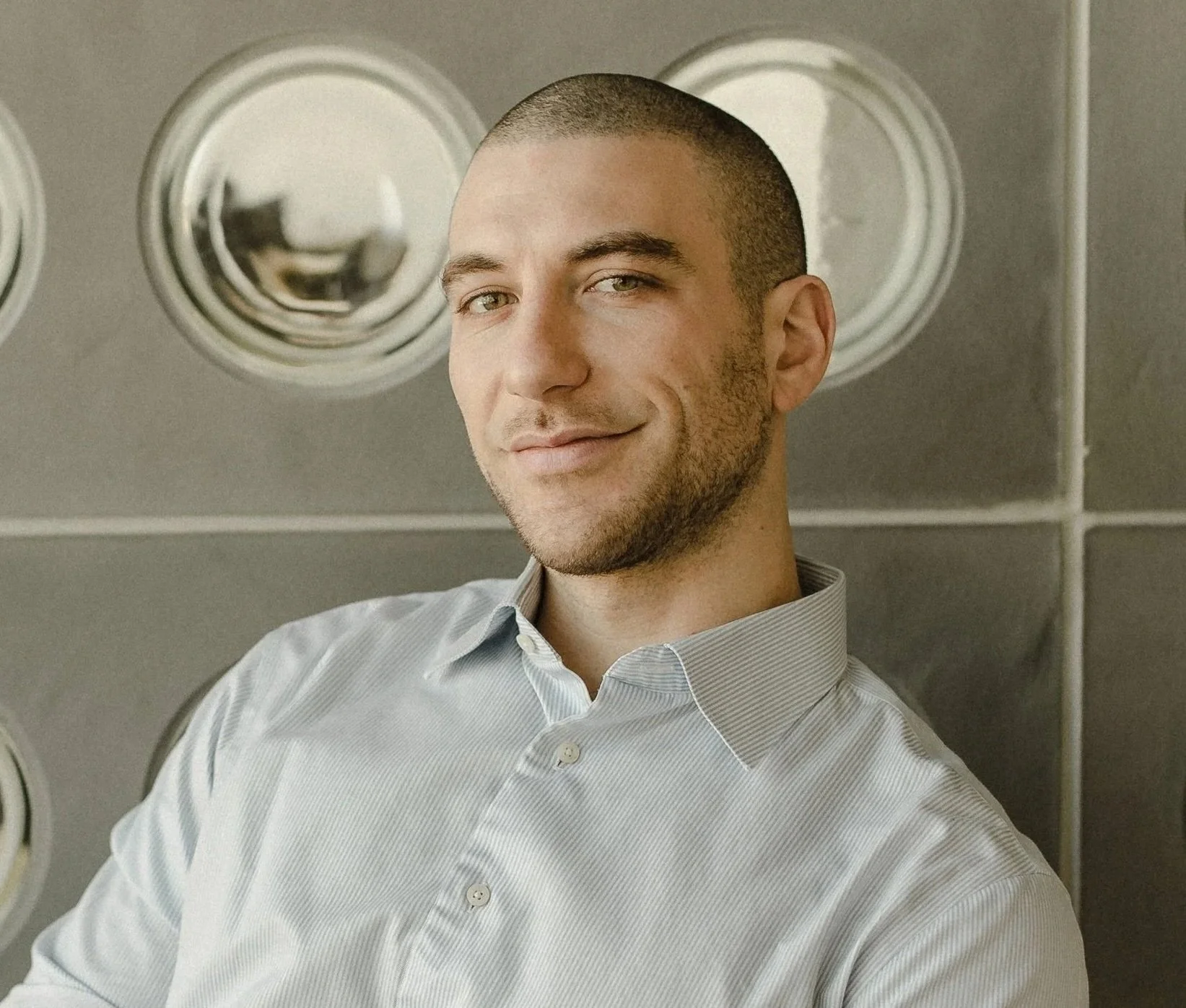 Portrait of a male lawyer in a light blue dress shirt, seated and smiling in front of a modern circular wall.