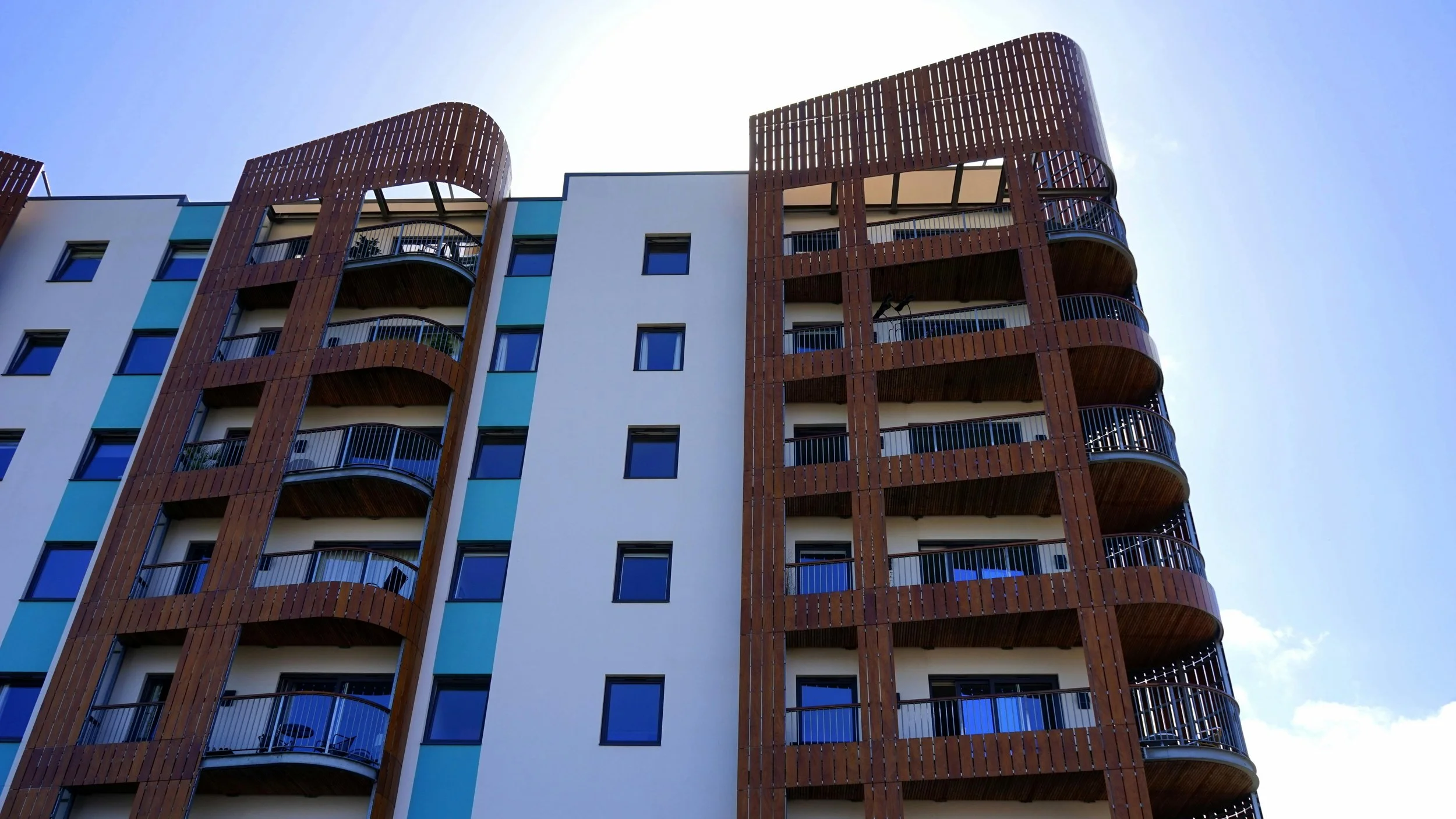Stylish white and brown/red apartment buildings with blue sky background and sun peaking over top.