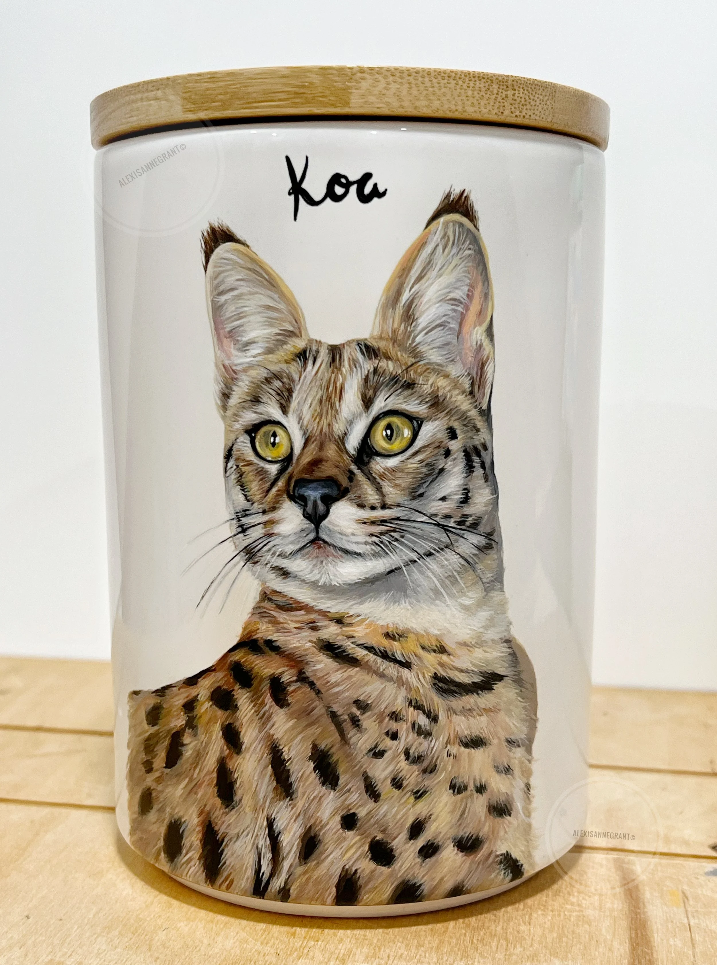 custom big cat portrait on ceramic urn with wood lid beautiful large ears and spots with his name painted above him on a white ceramic jar with wood lid