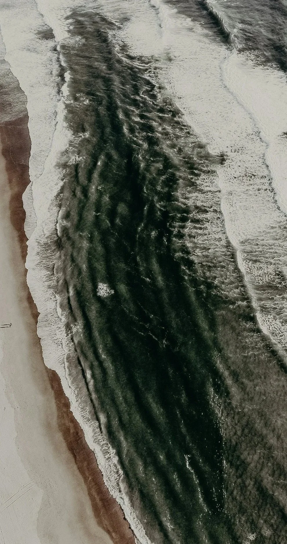 Aerial view of a beach with dark waves crashing onto the sandy shore.