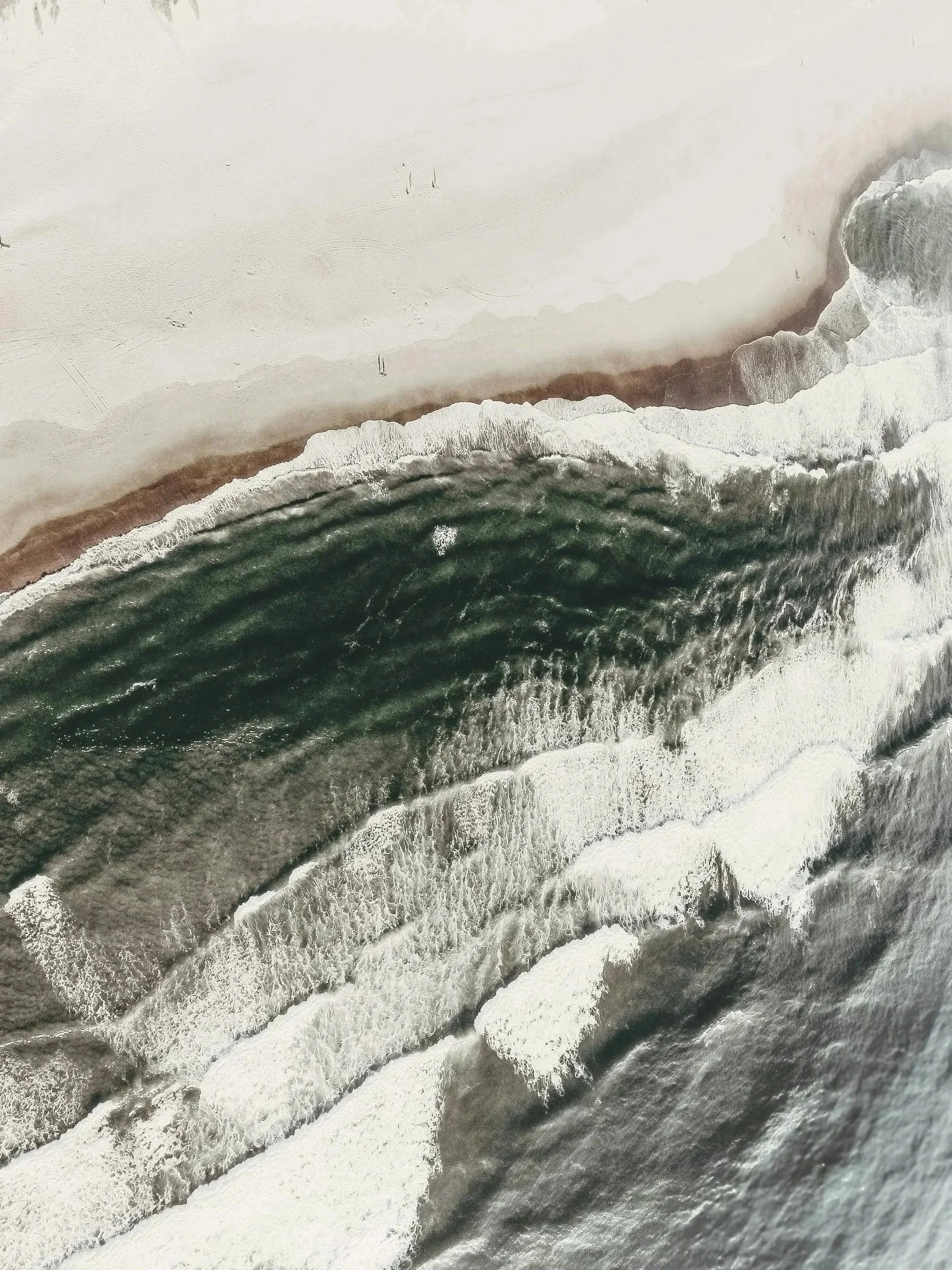 Aerial view of waves crashing onto a sandy beach with rocks.