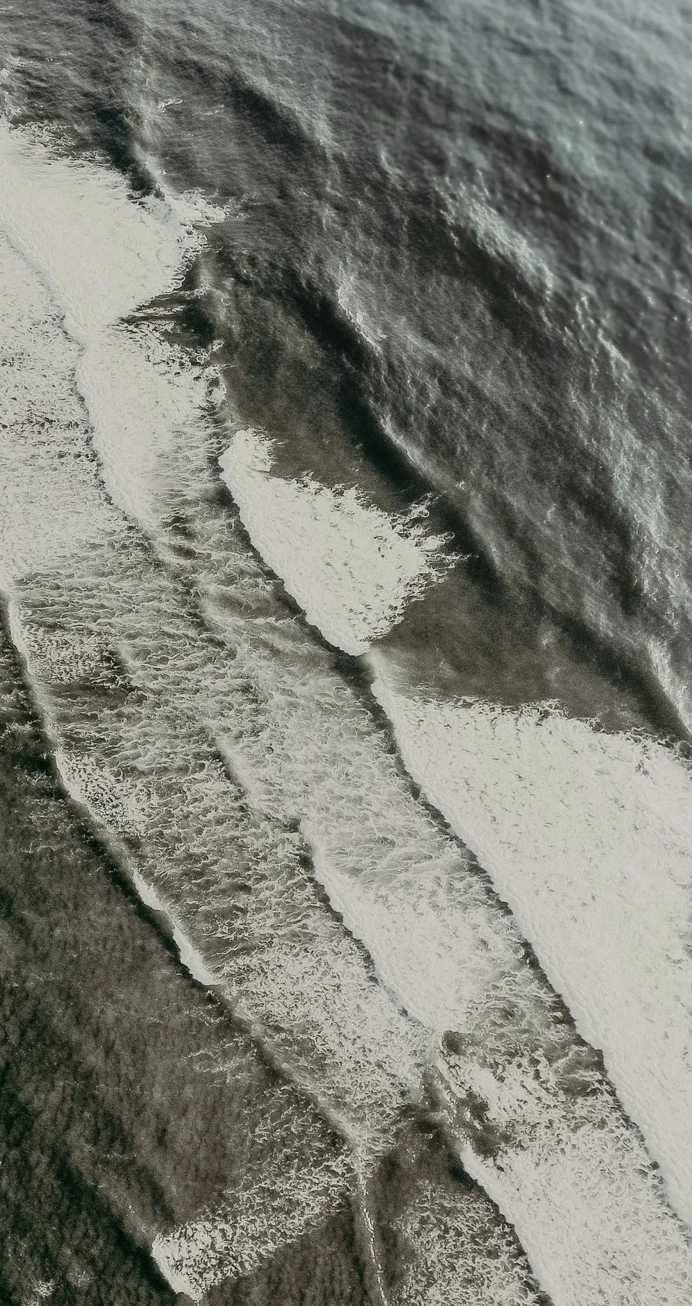 Aerial view of a beach with waves crashing onto the shoreline in black and white.