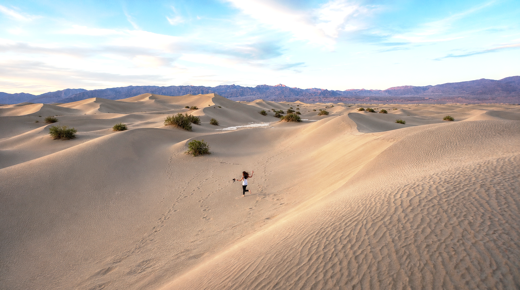 A person running on sand dunes in a desert landscape with mountains in the background during daytime.