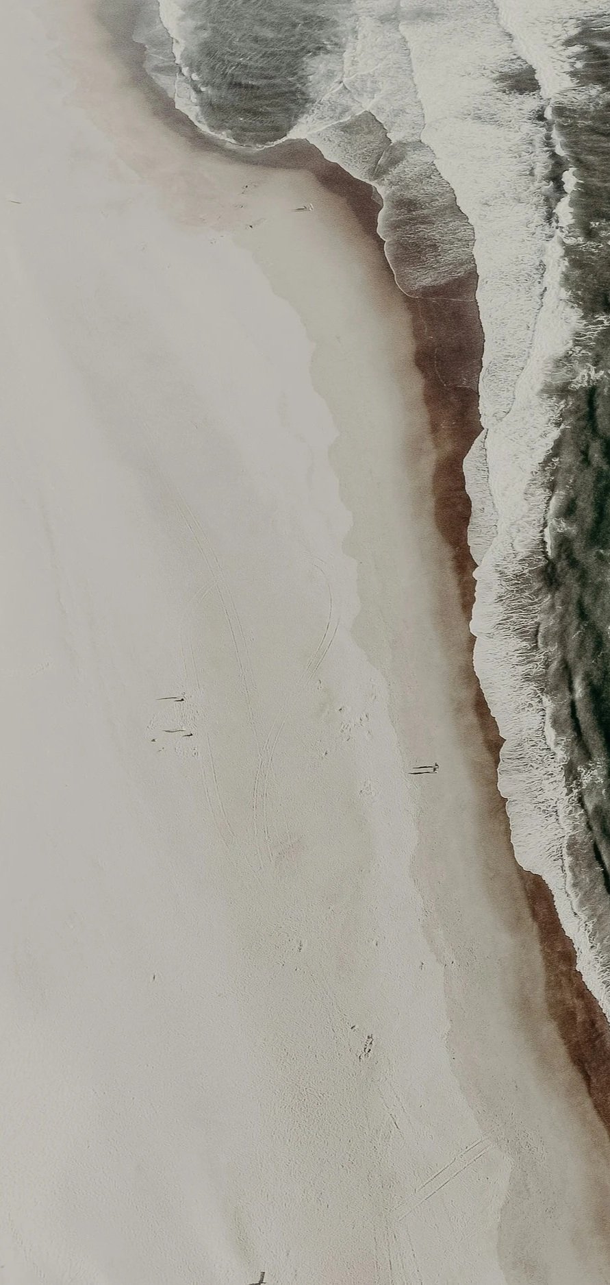 Beach with white sand and waves crashing onto the shore, a few people walking along the water's edge.