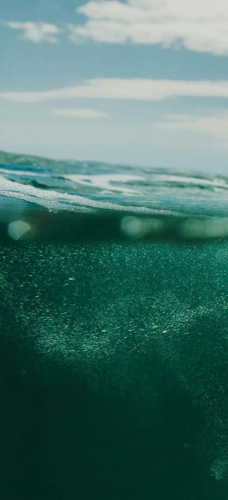Underwater view of the ocean with bubbles rising toward the surface and clouds visible in the sky.