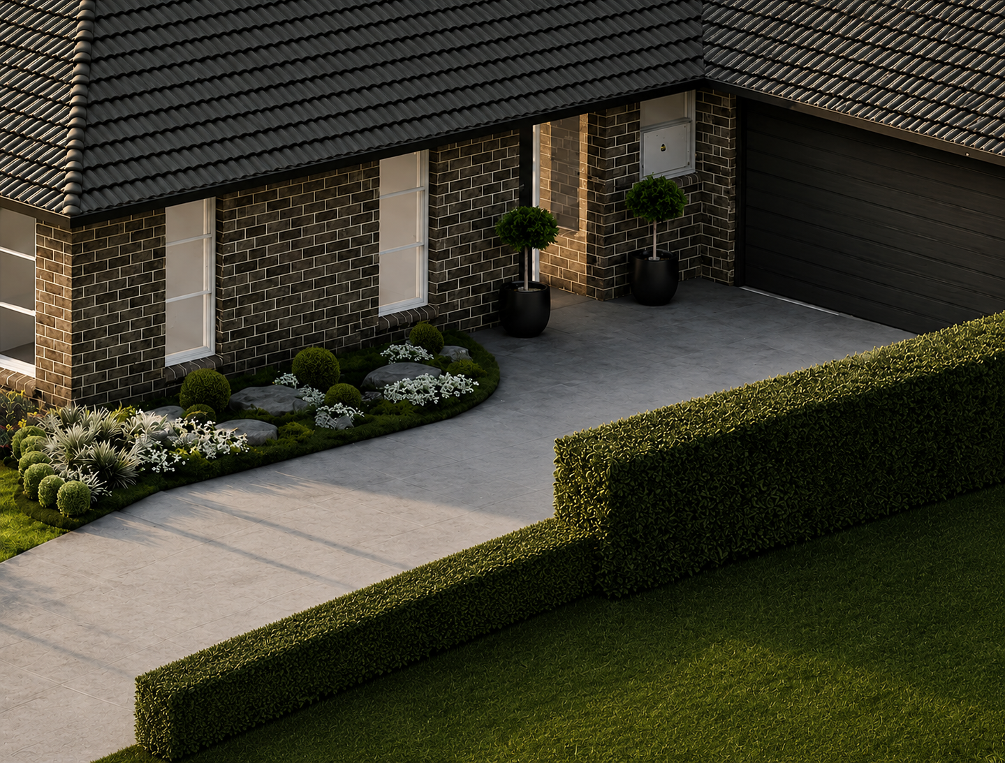 Front of modern house with brick exterior, black garage door, potted trees, landscaped garden with white flowers and bushes, and a concrete pathway.