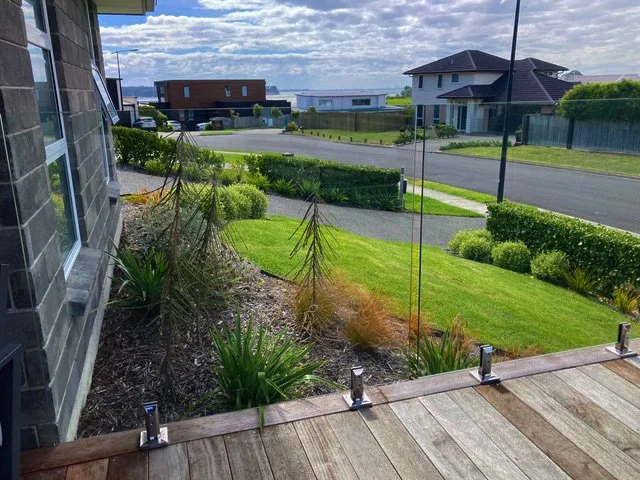 View of a balcony overlooking a residential neighborhood with houses, a street, and a green lawn under a partly cloudy sky.