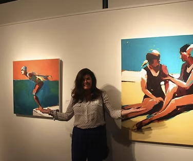 Person standing in art gallery between two colorful paintings of children playing