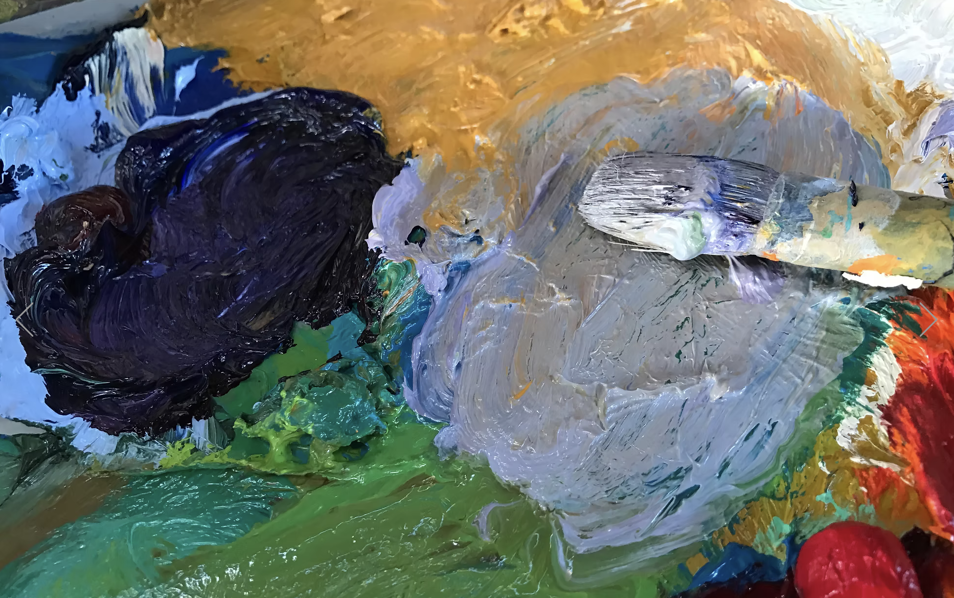 Close-up of thick, colorful oil paints on a palette, with a variety of dark, light, and vibrant colors, and visible brushstrokes.