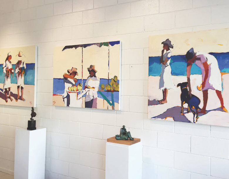 Art gallery featuring paintings of women and a dog on the beach, with sculptures displayed on white pedestals.