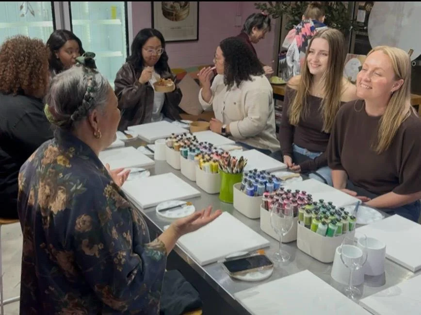 Group of women participating in a painting or craft class around a table with art supplies.