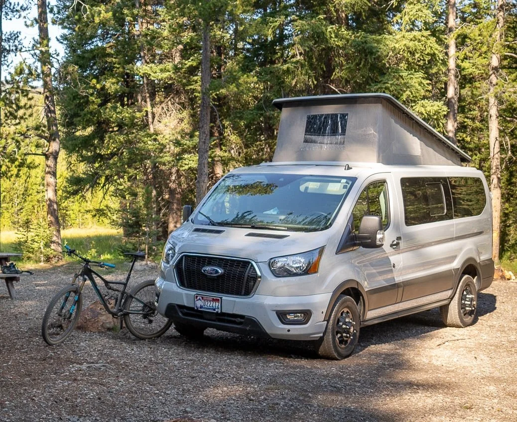 Grey Ford Transit in the wilderness, with a pop-top roof
