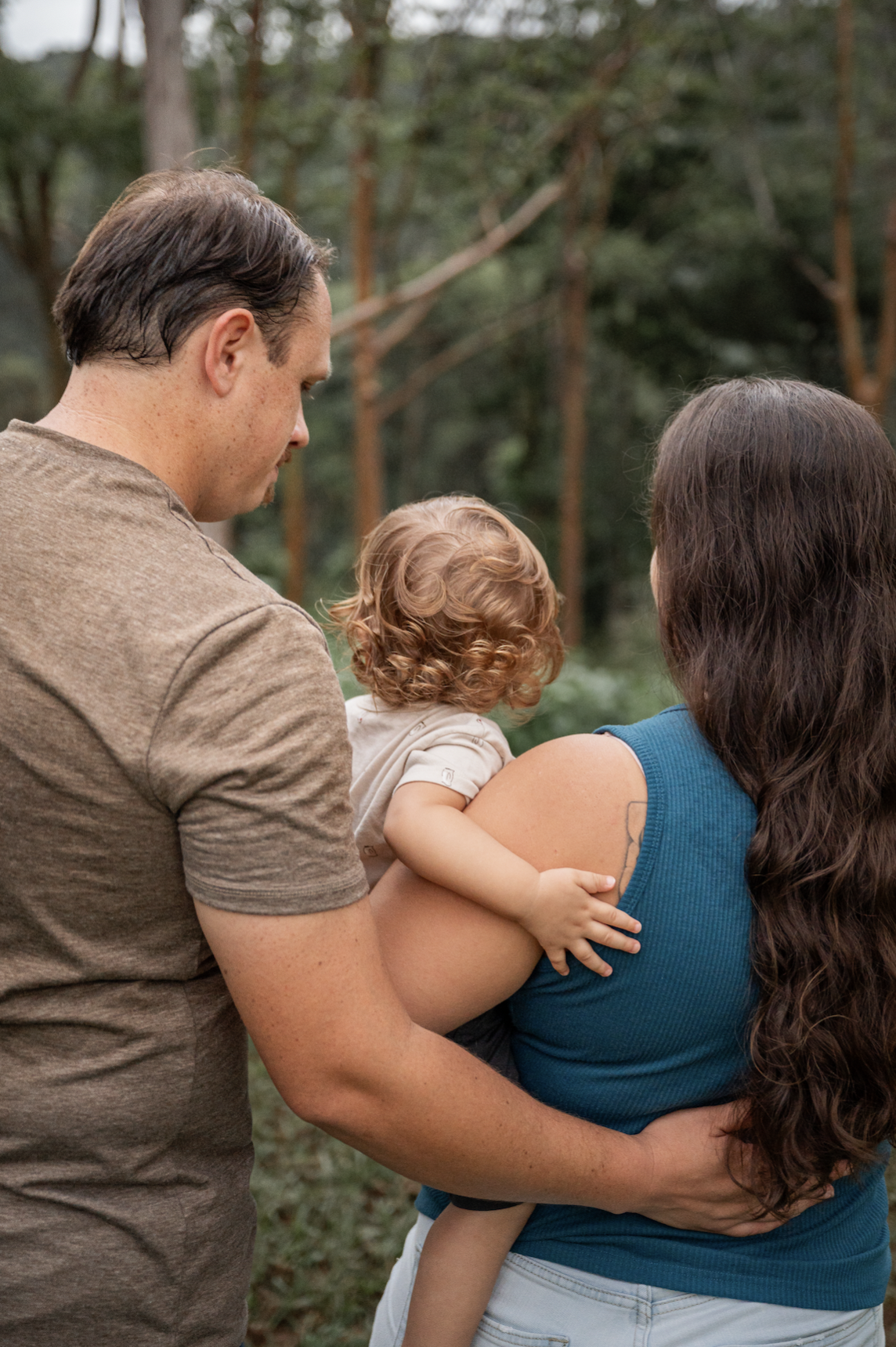 Family of three in a backyard with trees, with a man, woman, and young child, focusing on the child being held.