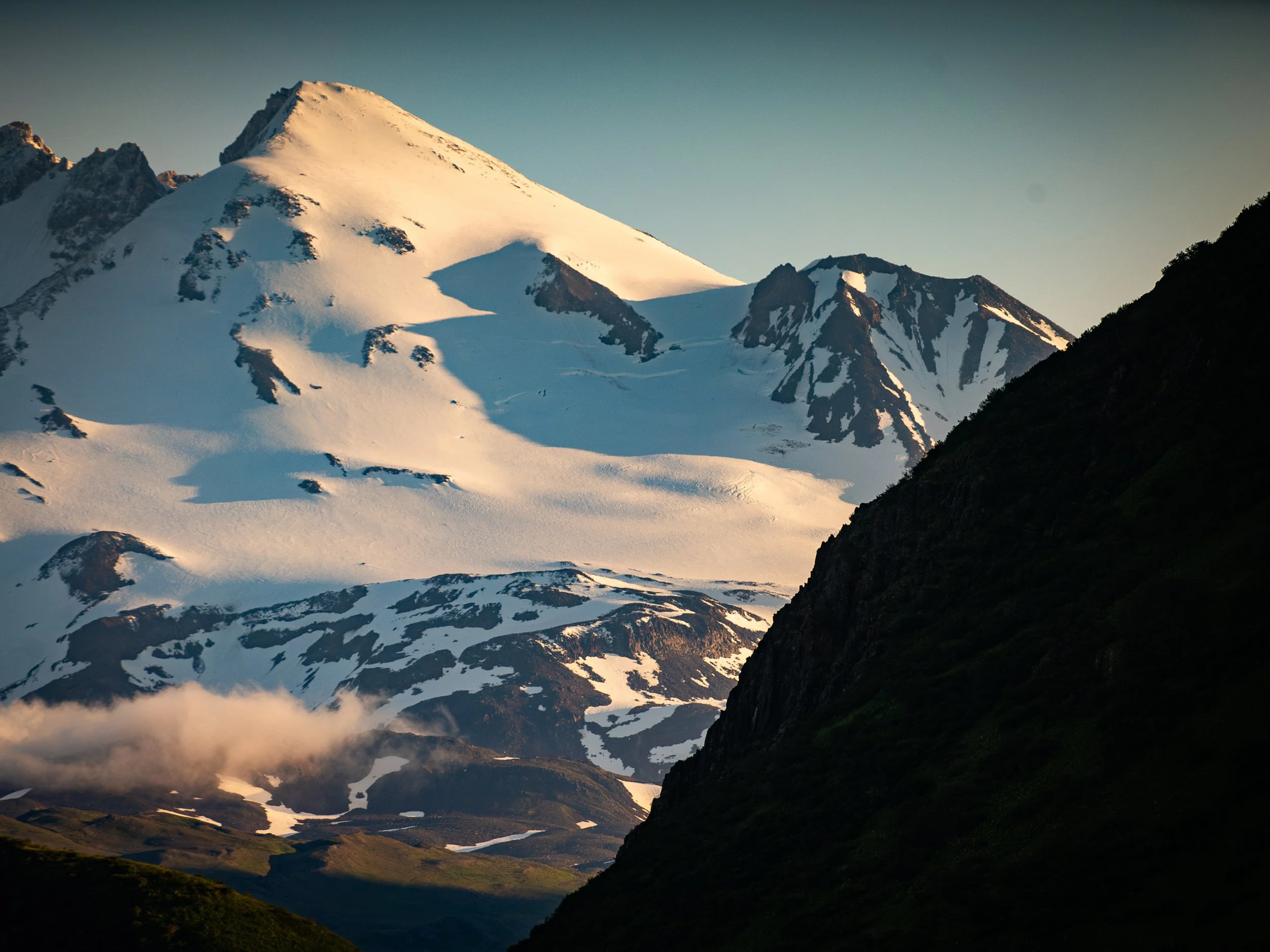 Snow-covered mountain peaks at sunrise with a dark valley in the foreground.