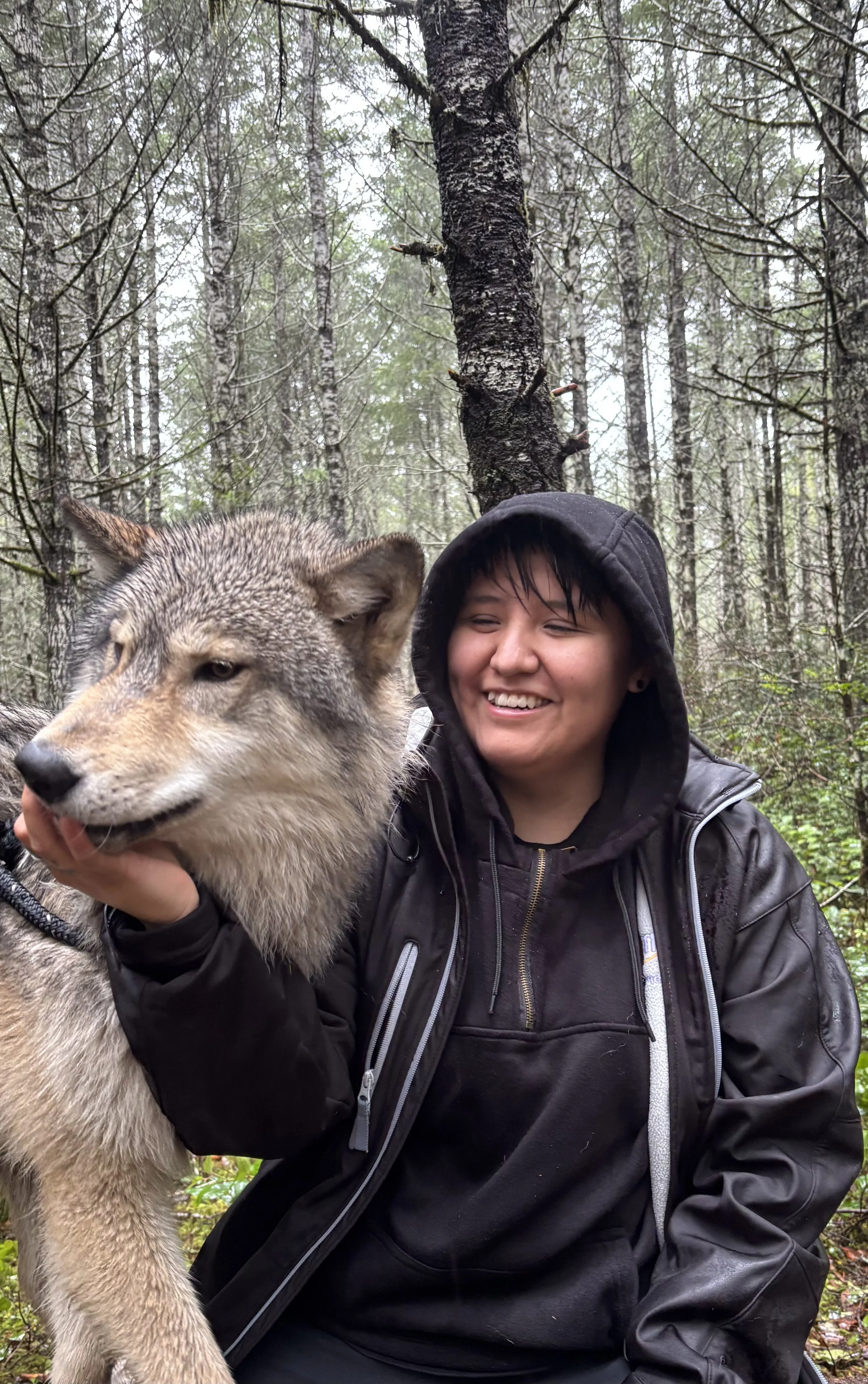 SeaJay Justice smiling while sitting beside a wolf and feeding it during a visit to a wolf sanctuary while filming a project.