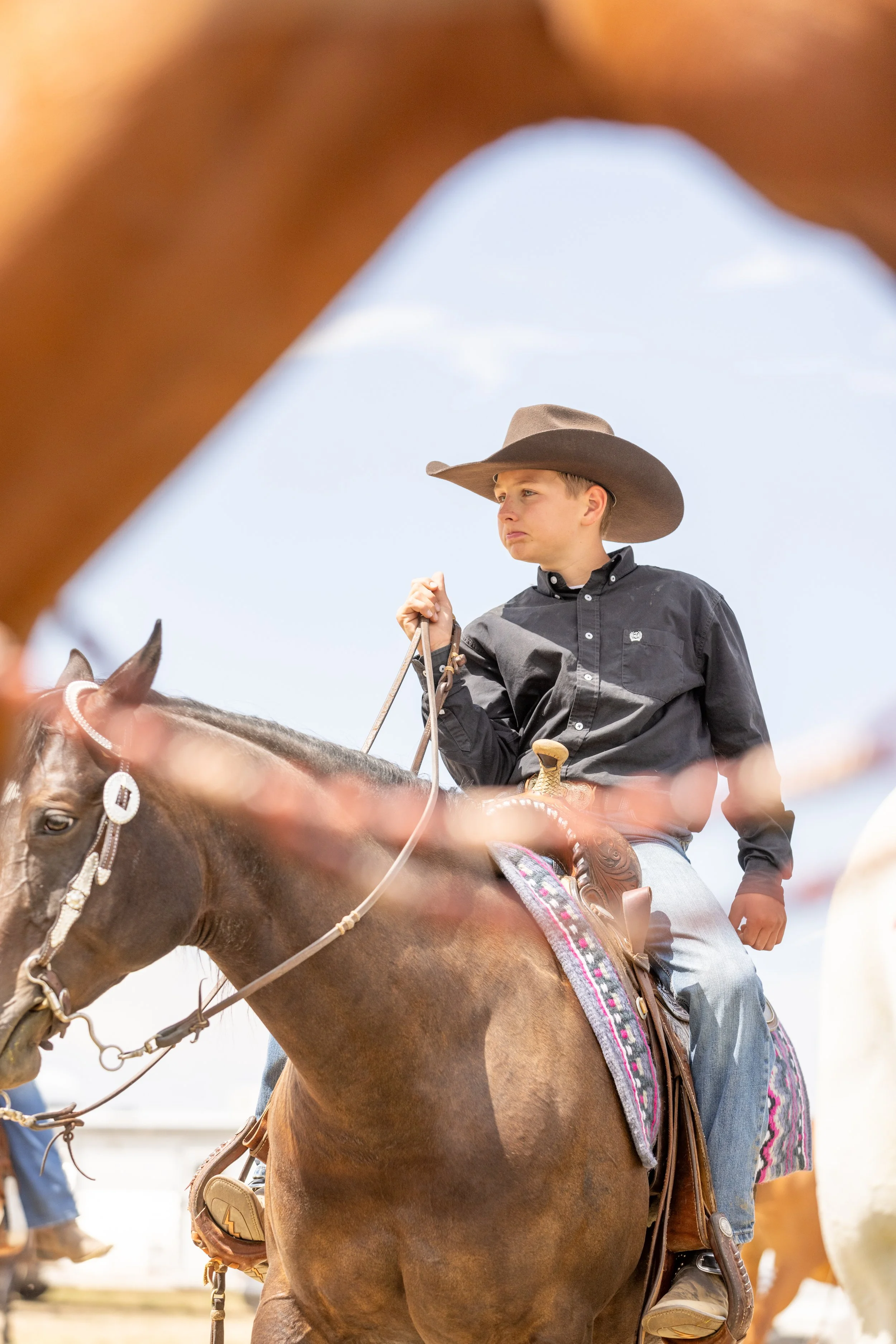 Young boy riding a horse, wearing a cowboy hat and a black shirt, holding the reins, sky in the background