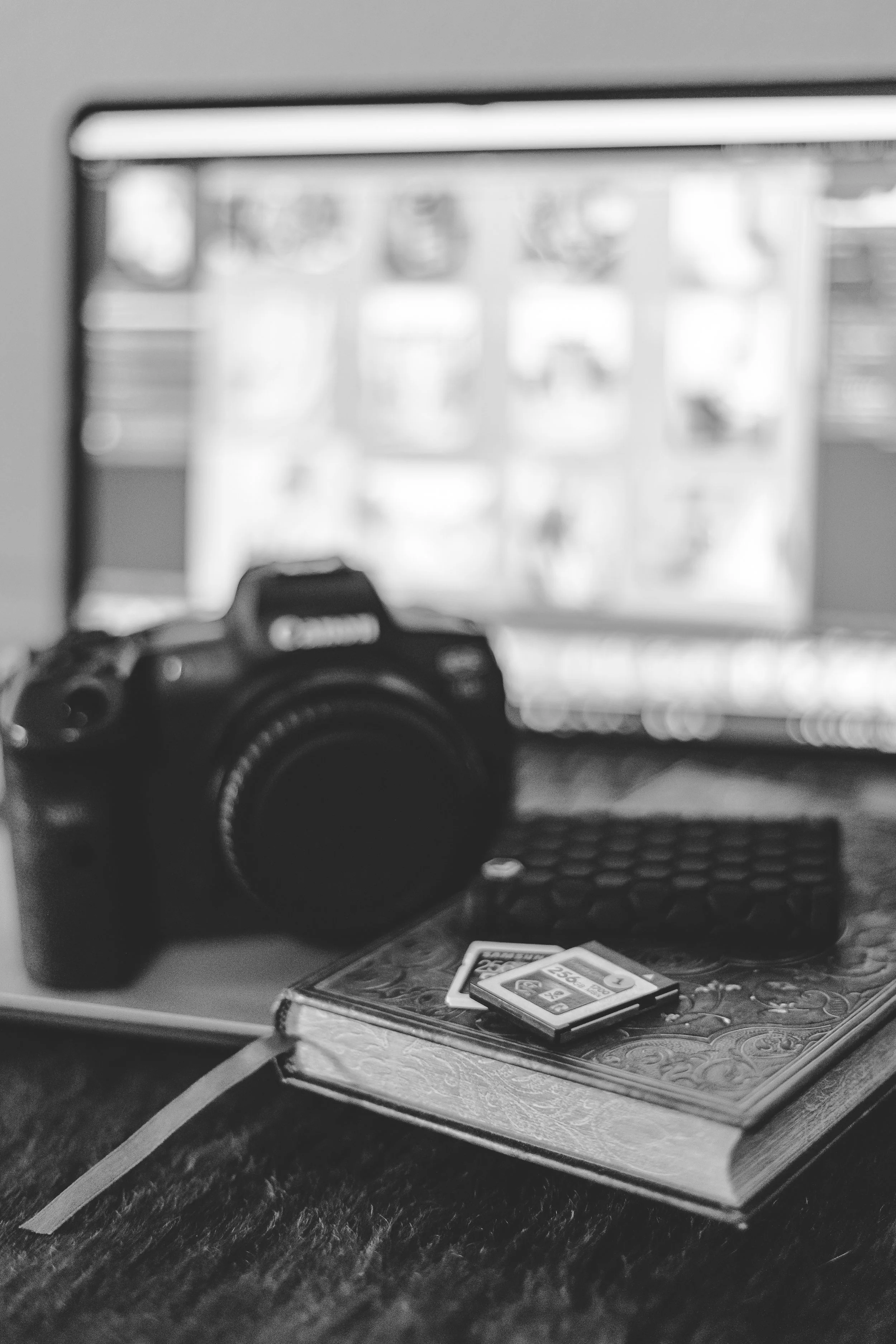 A blurry photo of a camera, poker cards, and bingo cards on a table with a computer screen in the background.