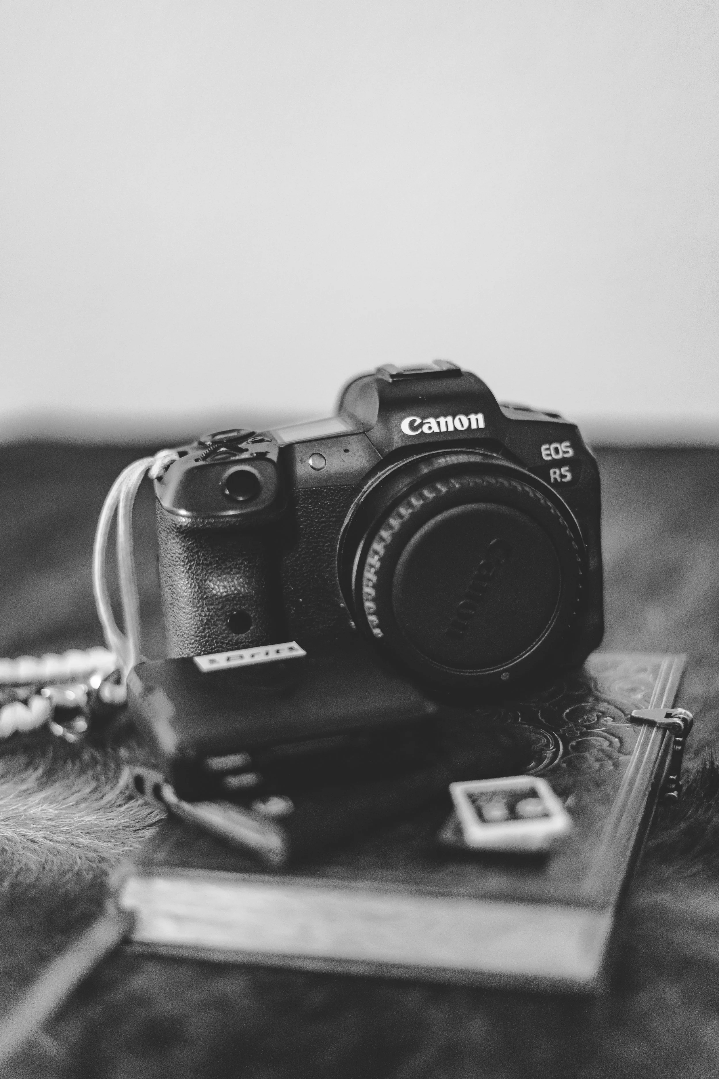 A black Canon EOS R5 camera placed on a table with various objects nearby in a black-and-white photo.