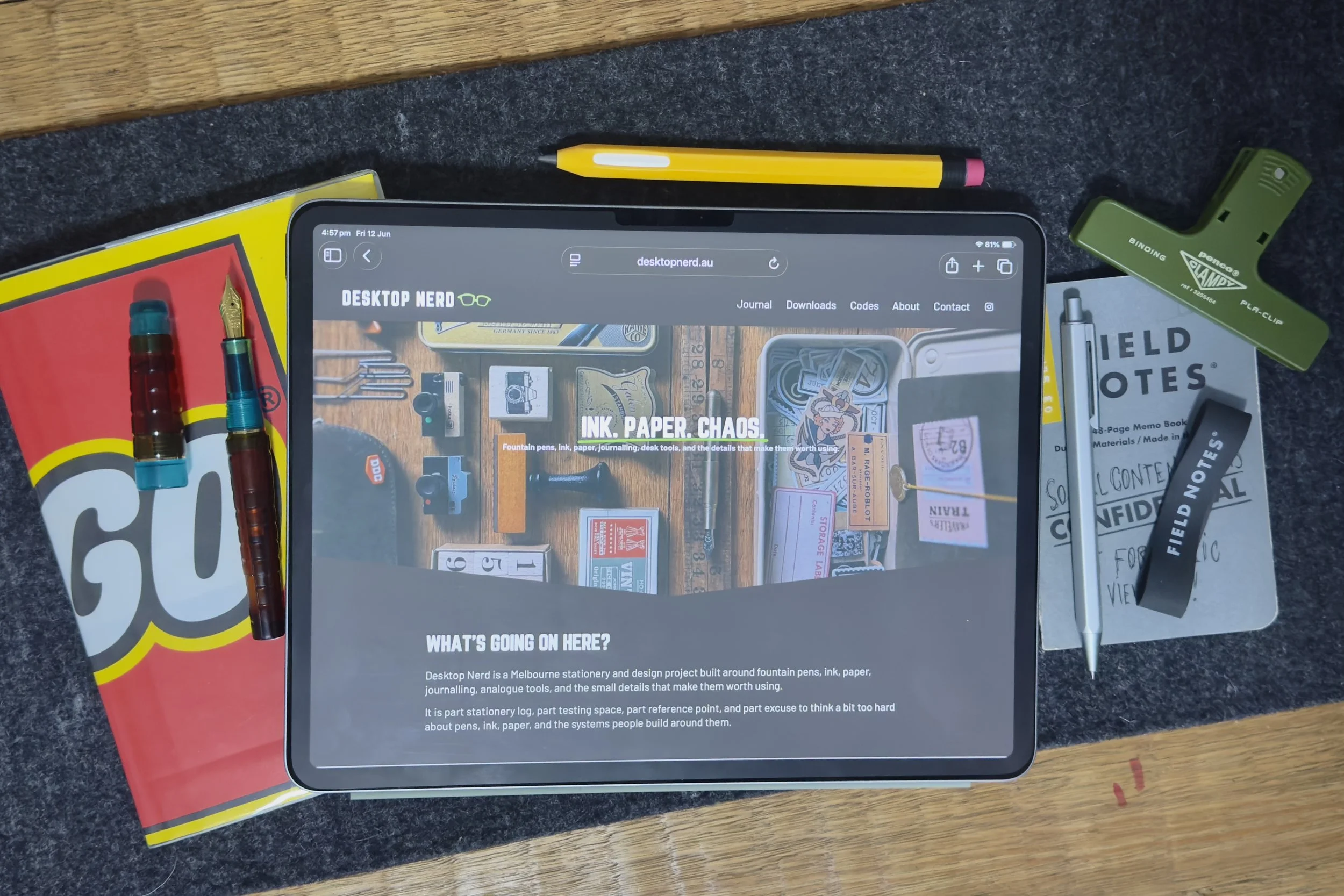 iPad displaying the Desktop Nerd website homepage surrounded by fountain pens, notebooks, Field Notes, pencil, and stationery tools on a desk.