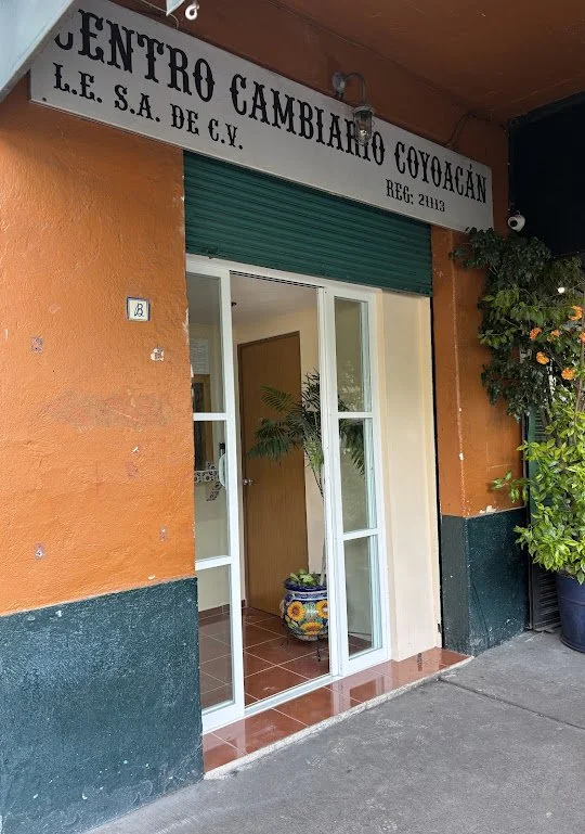 Entrada de un centro de cambio en Coyoacán con cartel en la parte superior y plantas decorativas afuera.