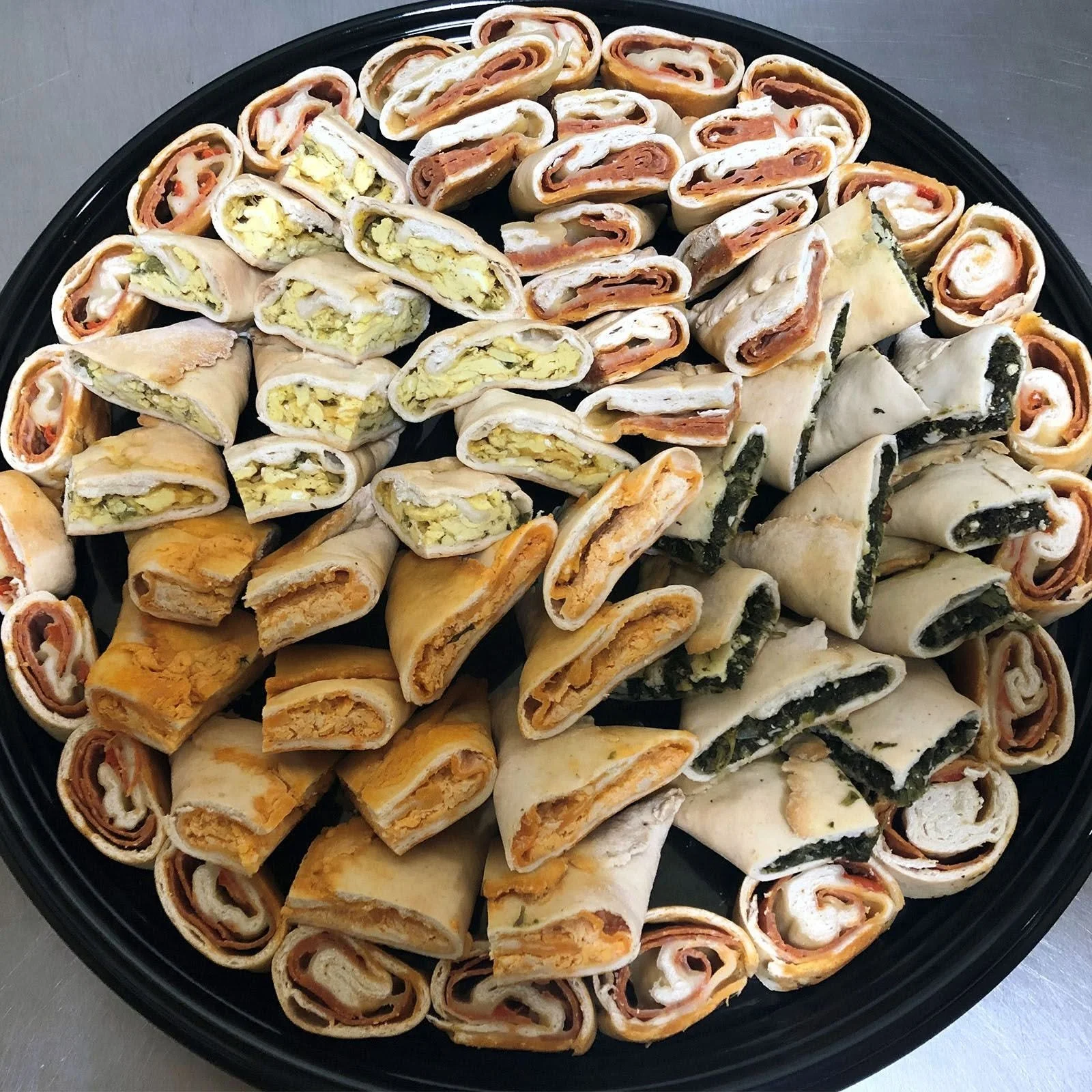 Assorted pinwheel sandwiches with various fillings, arranged on a black tray.