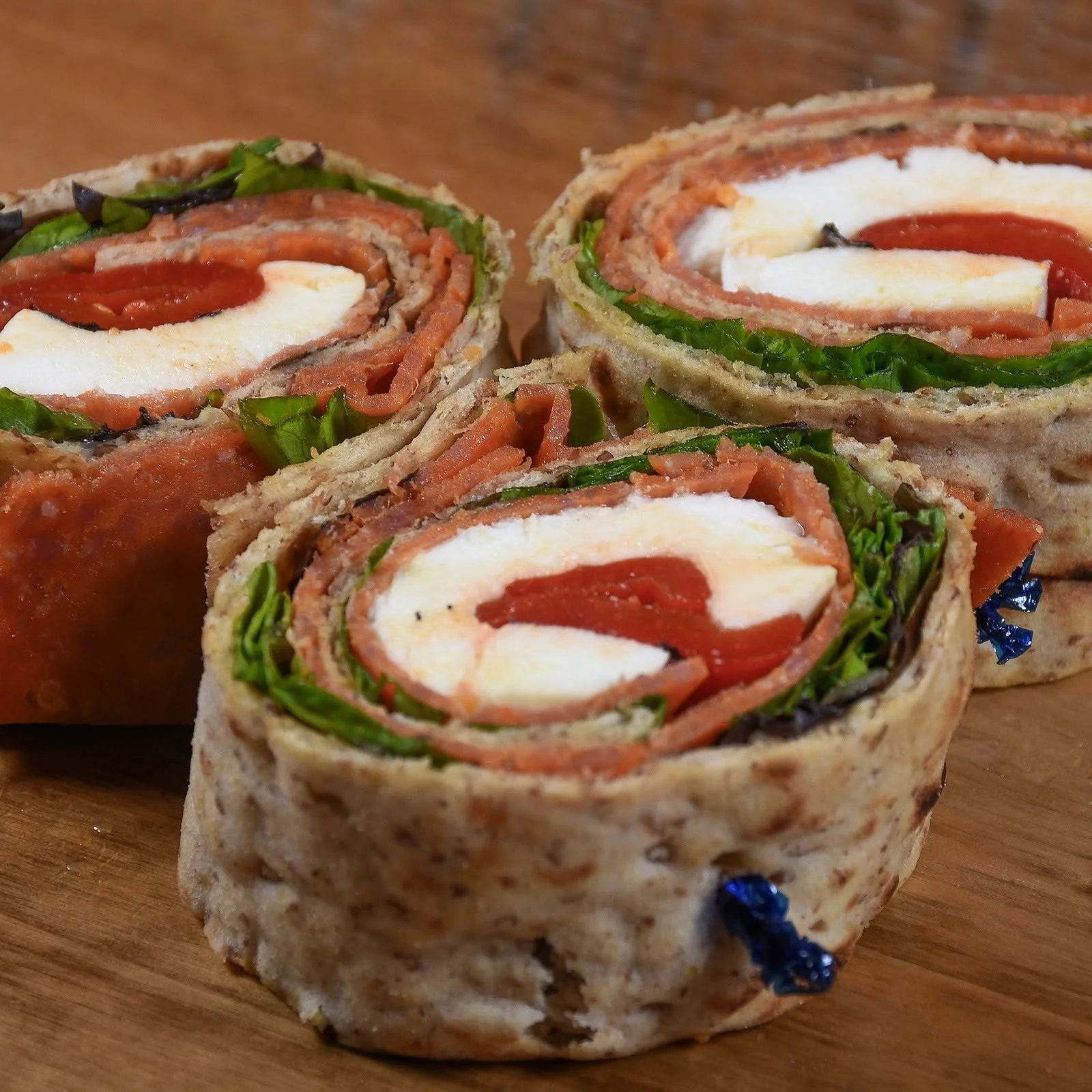 Close-up of three veggie wraps cut in half, showing spinach, tomato, shredded meat, cheese, and other ingredients in a whole wheat wrap.