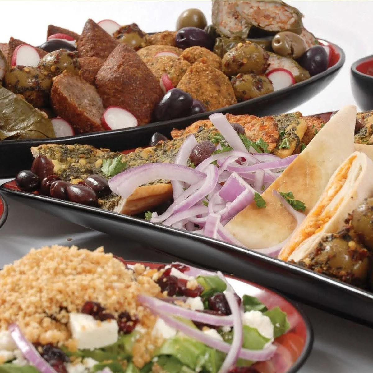 Assorted Middle Eastern dishes, including falafel, stuffed grape leaves, olives, tabbouleh, and pita bread, served on black platters.
