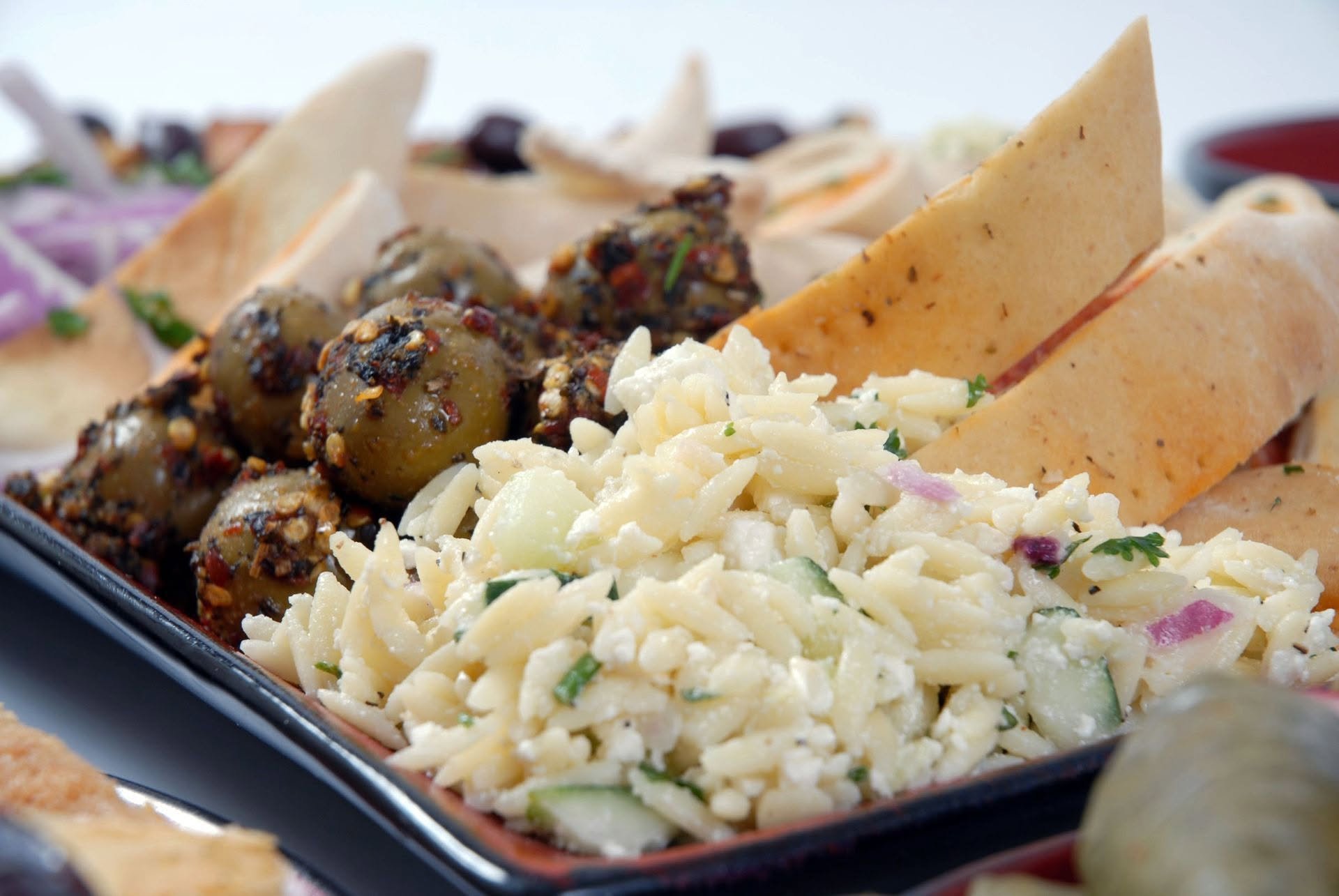 Assorted Mexican dishes on a black platter, including jalapeno peppers with seasoning, shredded cheese salad, and sides of chips and dip.