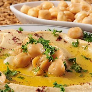 Hummus topped with chickpeas, chopped parsley, and drizzled with olive oil, with a bowl of chickpeas in the background.
