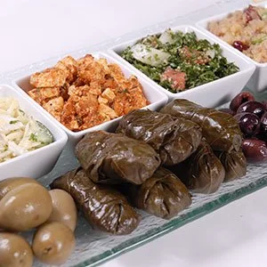 Assorted Mediterranean appetizers including stuffed grape leaves, marinated olives, and various dips or salads