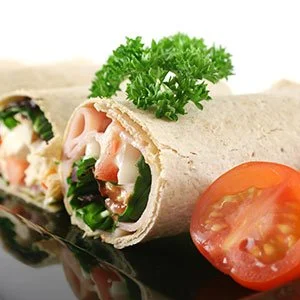 A wrap filled with lettuce, sliced turkey, and other ingredients, garnished with parsley, along with a slice of tomato.