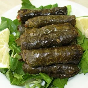 Six grape leaf-wrapped stuffed grape leaves on a bed of lettuce with lime wedges
