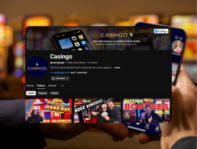 A person holding a smartphone displaying the Casingo YouTube channel page, featuring videos about casino bonuses and strategies, with a blurred background of slot machines.