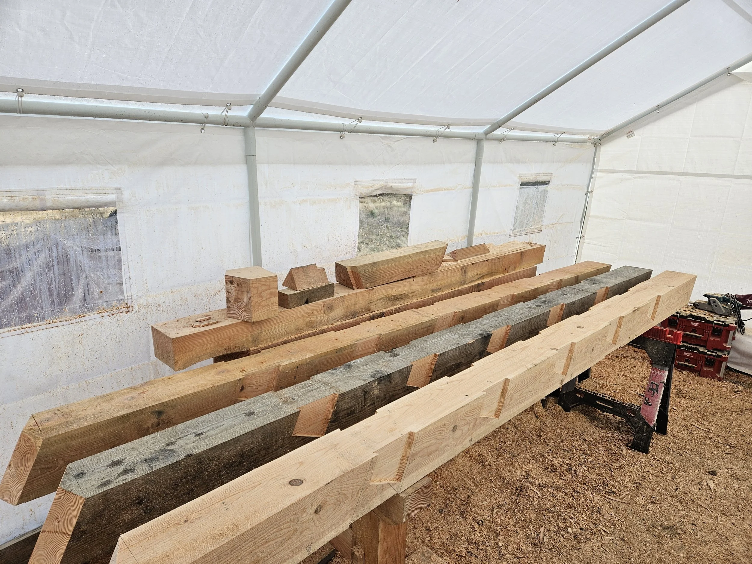 Interior of a greenhouse with wooden planks on work tables, and white fabric walls and roof held up by metal pipes.