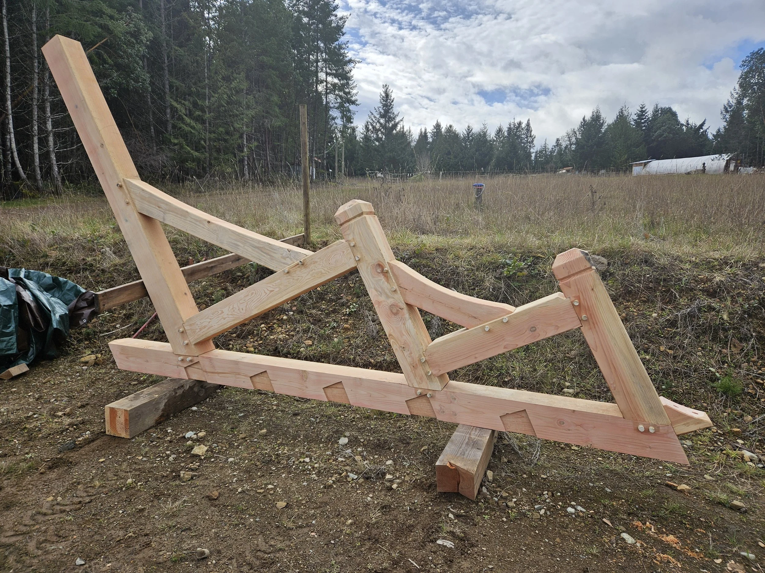 Wooden structure under construction in an outdoor rural area with trees and cloudy sky in the background.