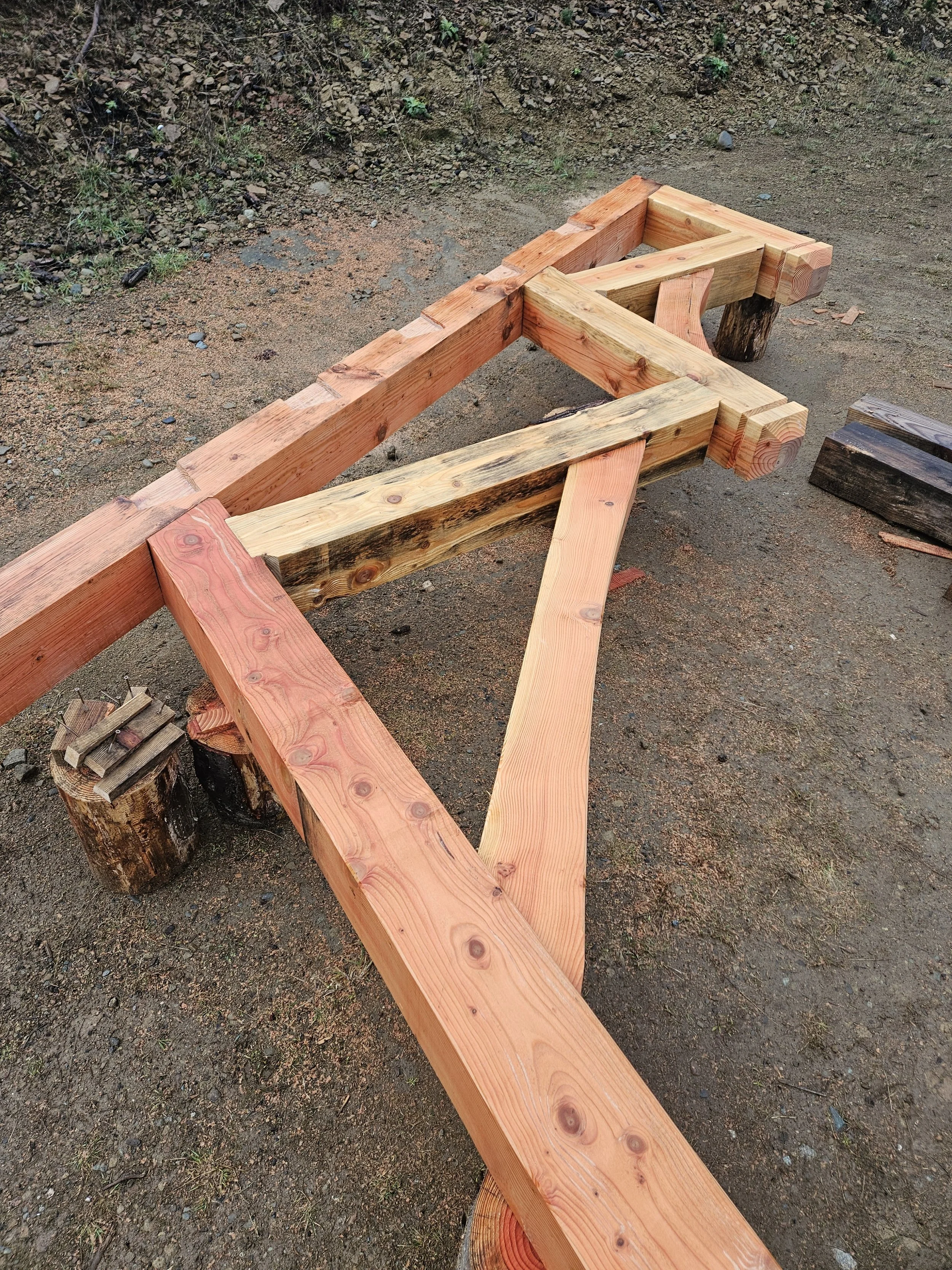 Wooden beams arranged on tree stumps and the ground, likely part of a construction or woodworking project outdoors.
