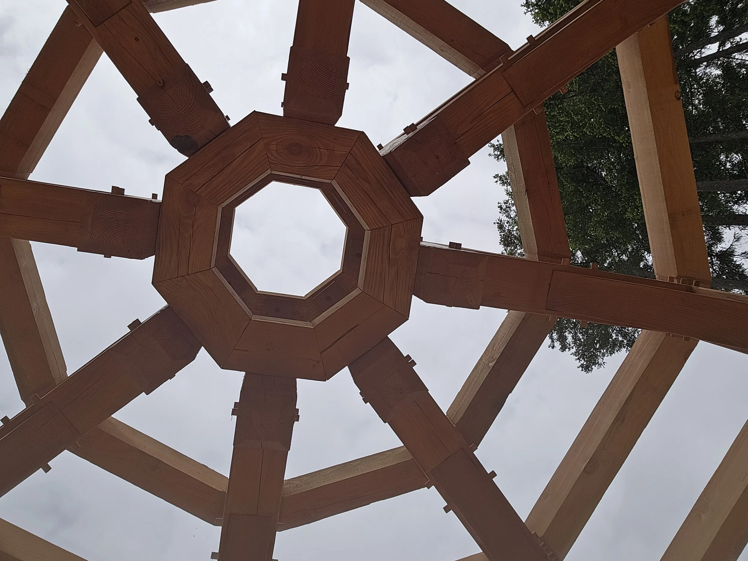 Close-up of a wooden structure under construction viewed from below, with the sky and trees in the background.
