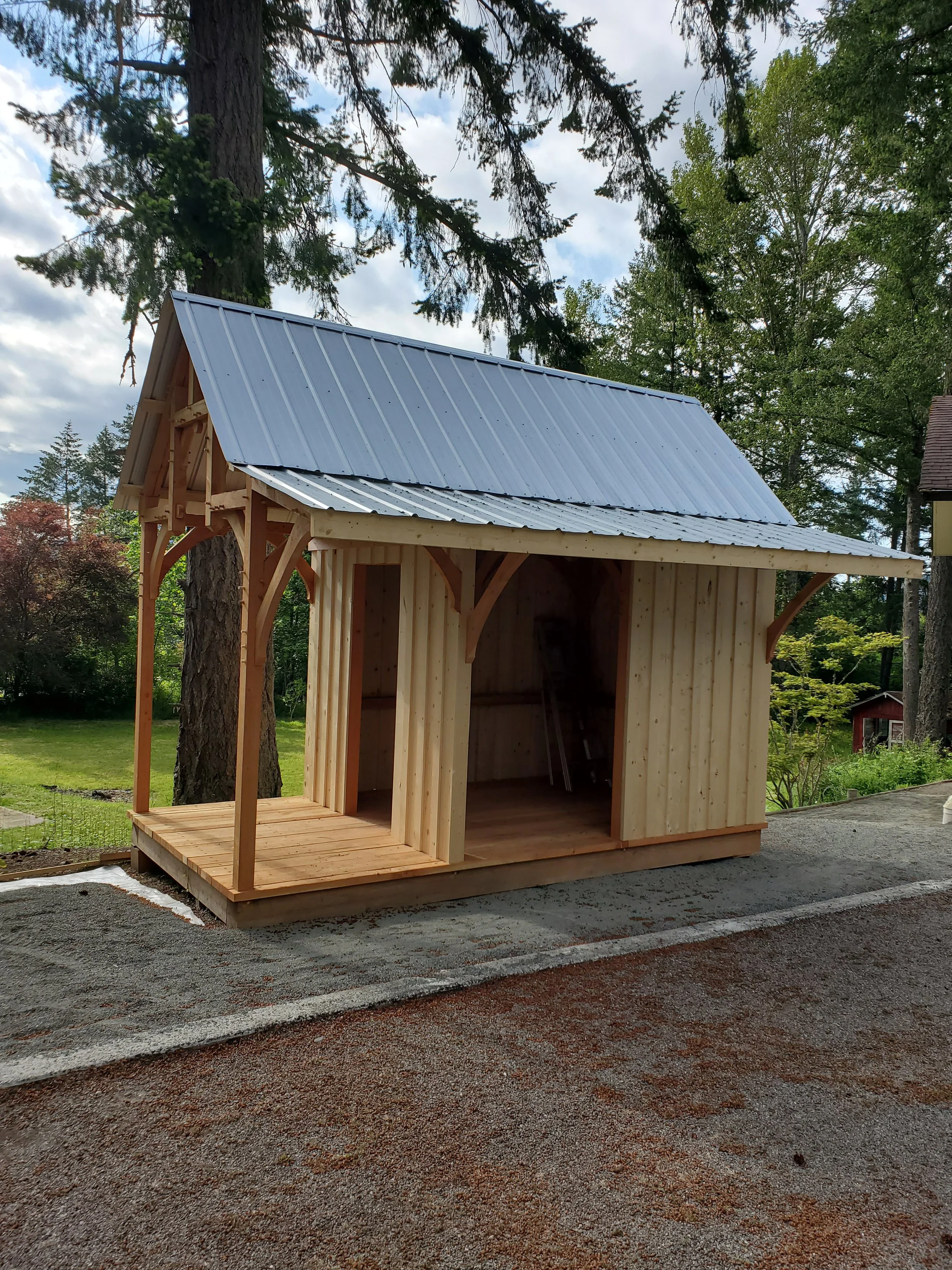 A small wooden structure with a metal roof, situated outdoors in a wooded area.