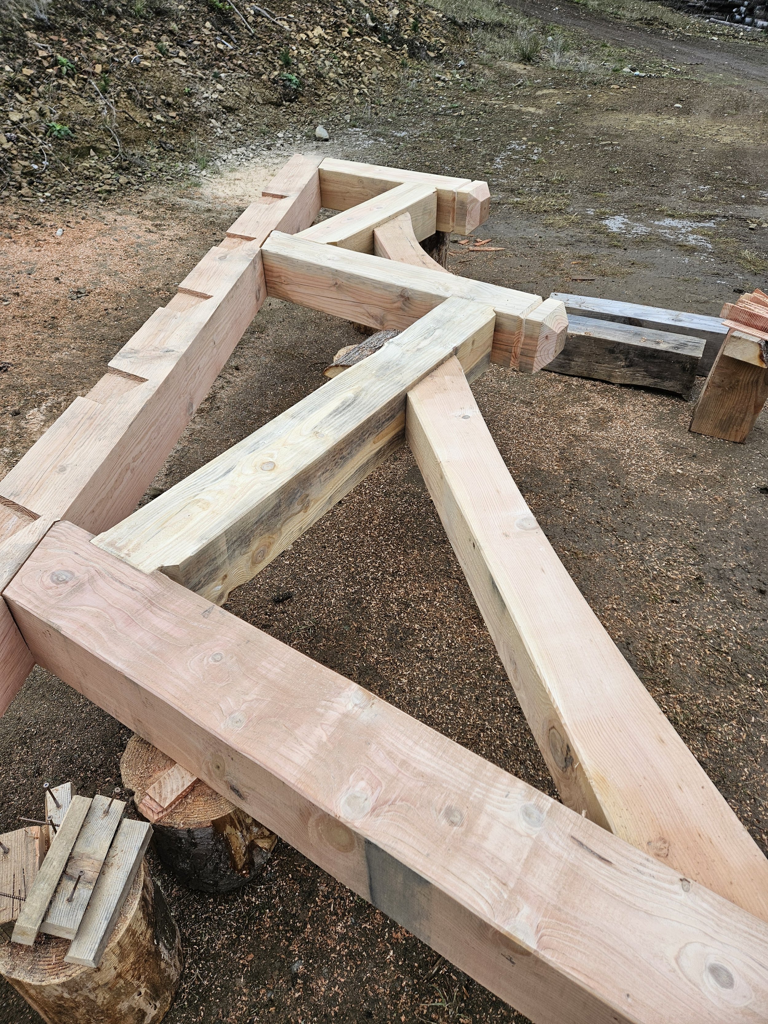 Wooden framework being built outdoors, possibly for a structure or fence, with tools and extra wood around.