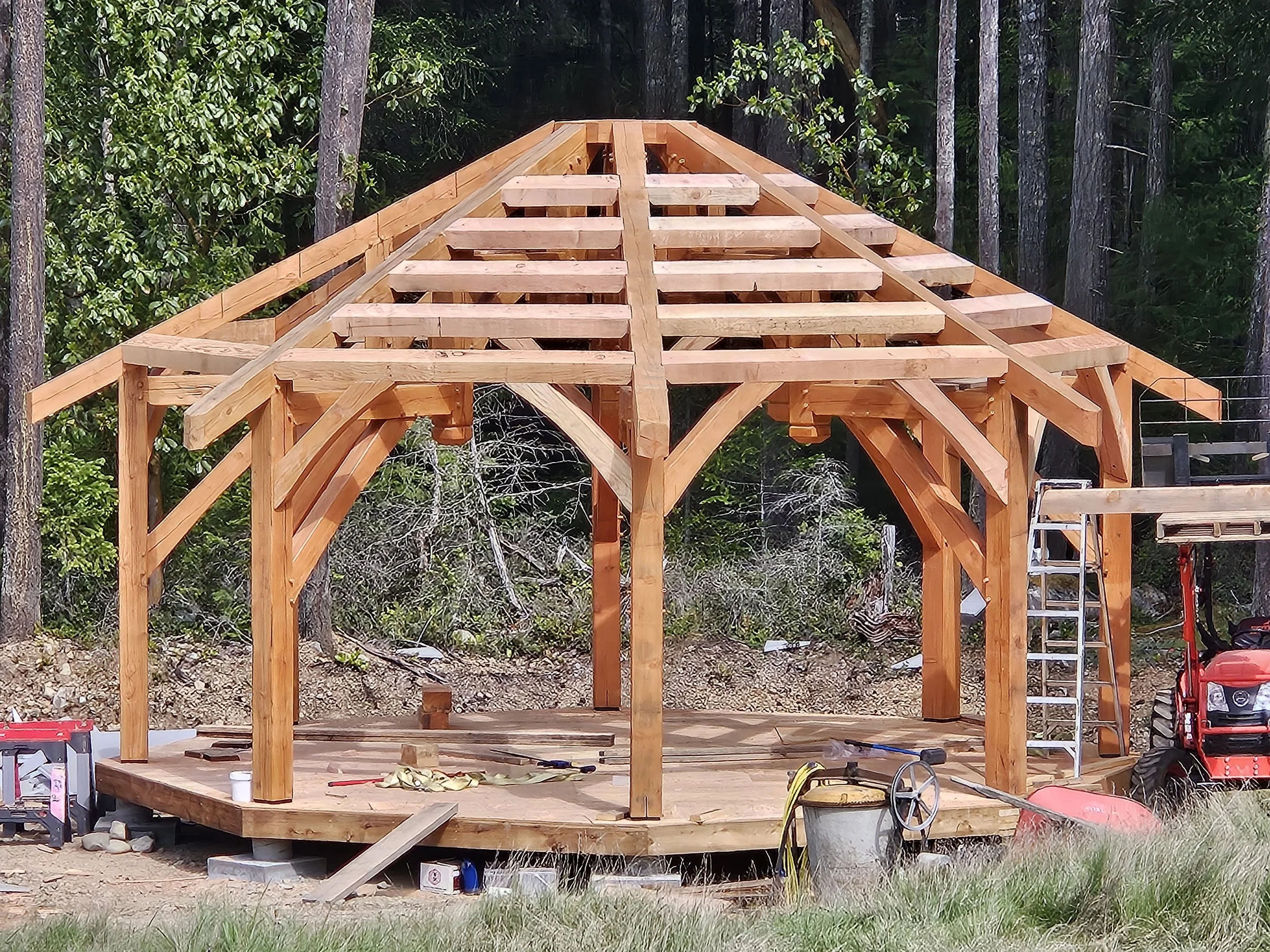 Wooden structure under construction in a forested area, with tools and equipment around it.