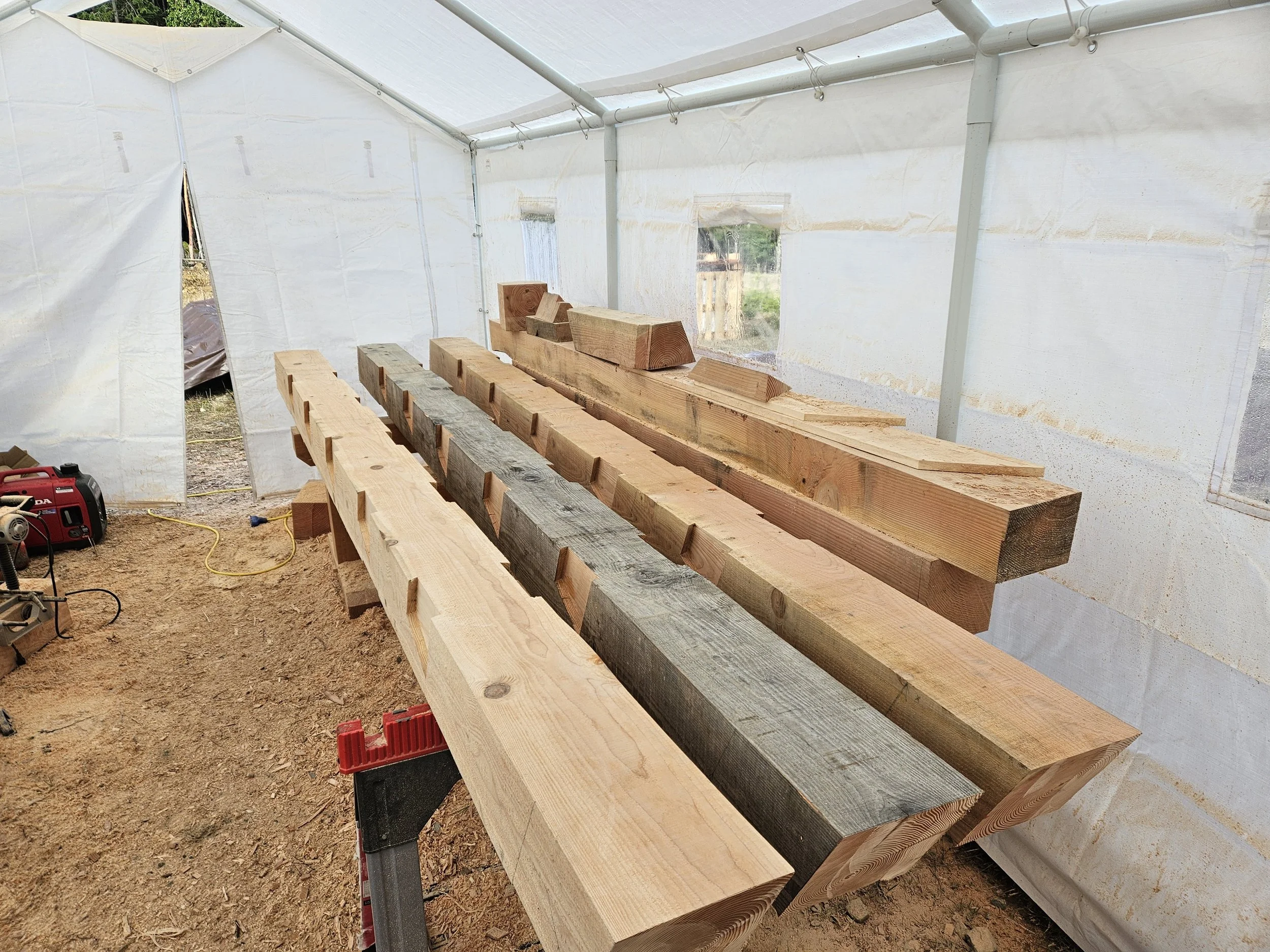 Wooden planks on a workbench inside a white enclosure under construction, with a red generator and tools on the ground.