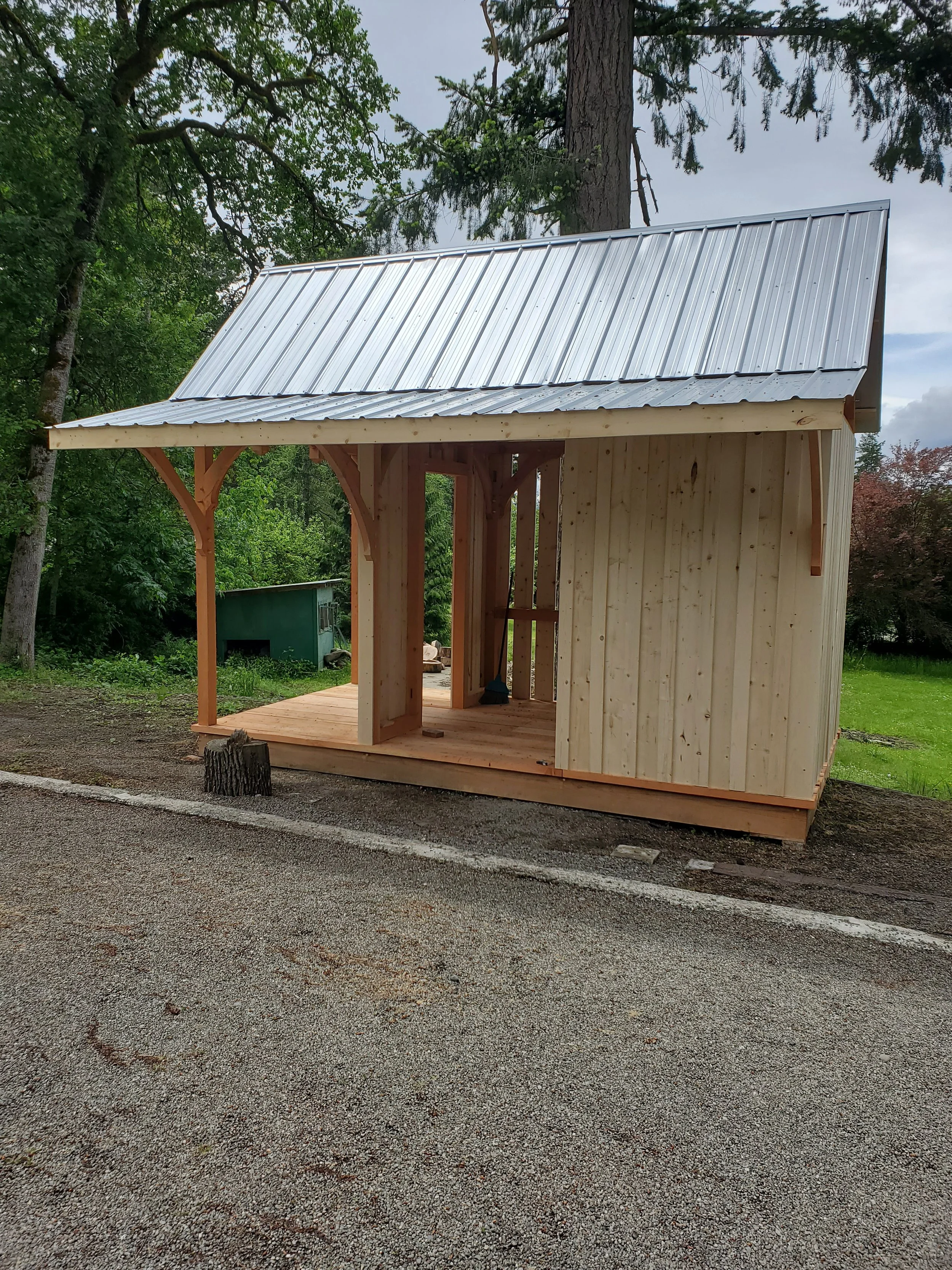 Timber bunkie under construction with a metal roof in a green outdoor area.