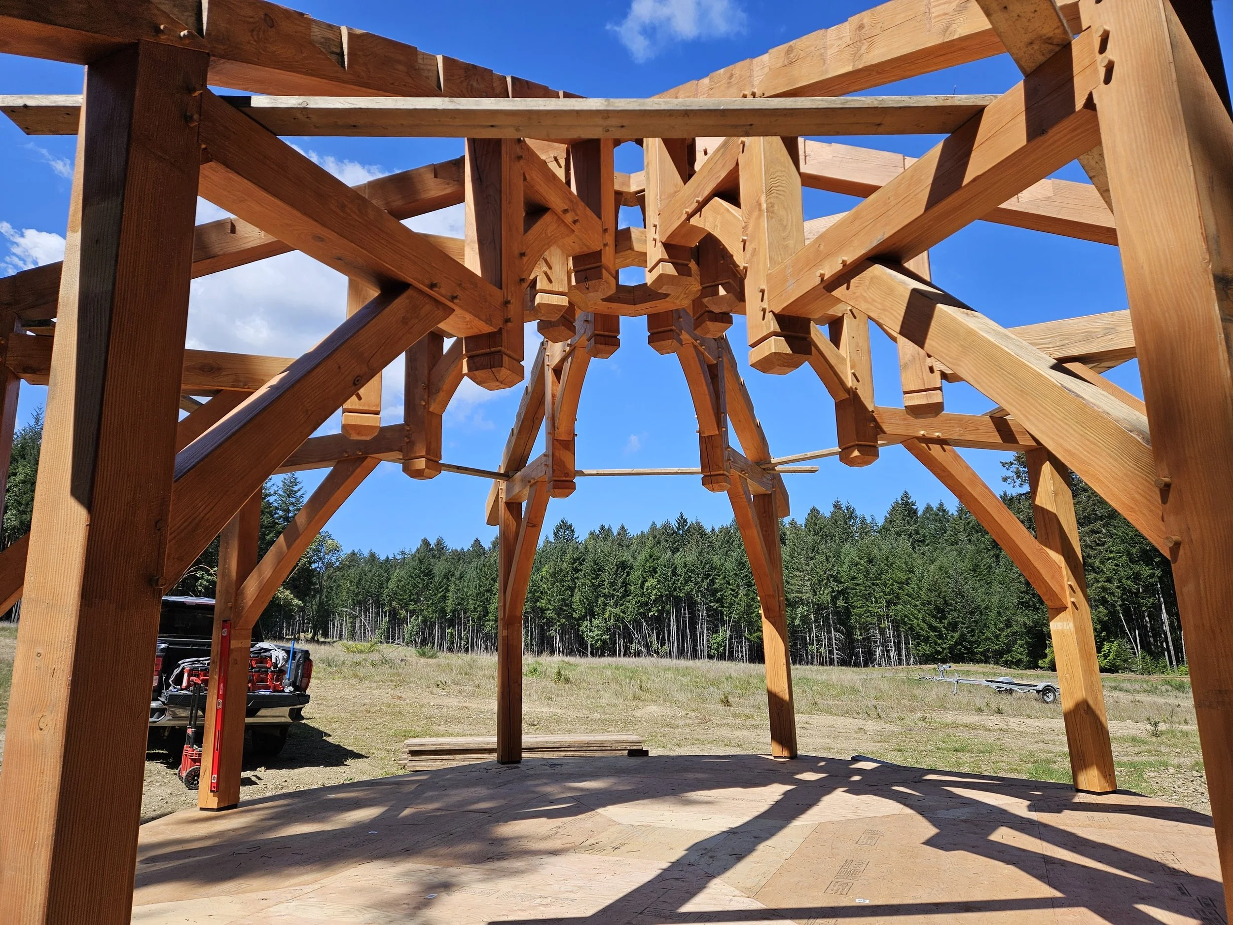 Wooden framing structure under construction with a blue sky and trees in the background.