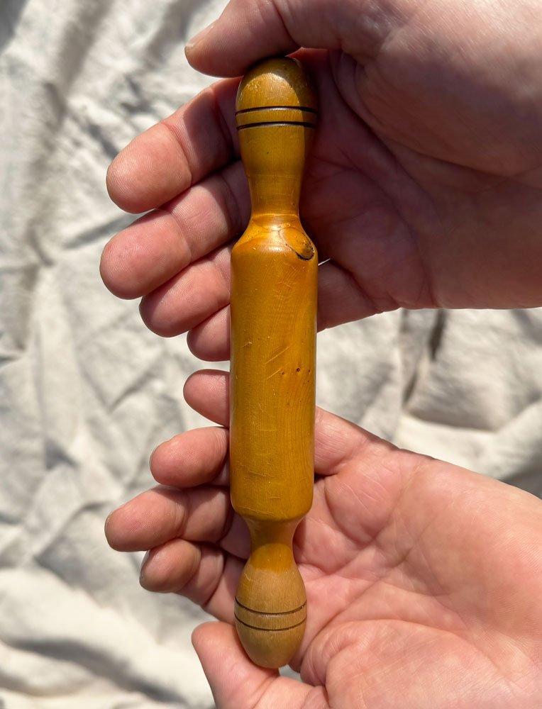 Andrew McNamara's hands holding a vintage wooden rolling pin with a light brown finish and black decorative rings at each end.