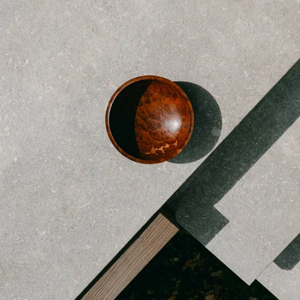 Top view of a round Red Mallee Burl wooden bowl on a gray concrete surface with a long shadow cast by the bowl.