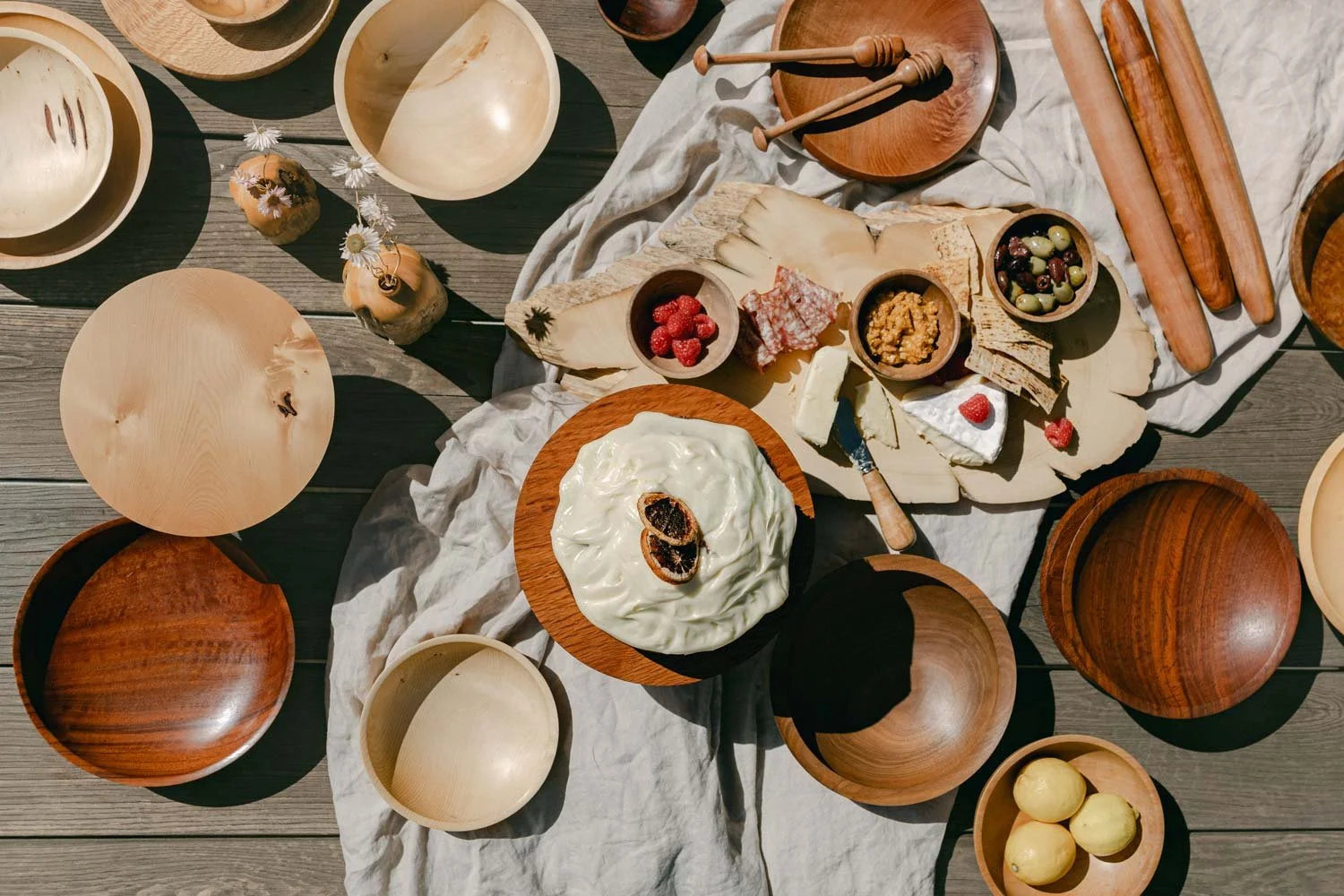 An outdoor spread of cheese, fruit, and snack bowls on a timber floor with multiple timber homewares made by Andrew McNamara Woodturning.
