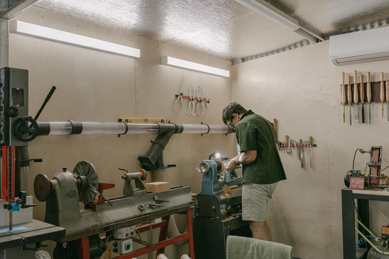 Australian wood turner, Andrew McNamara, working with a lathe machine in his woodturning workshop, surrounded by woodworking tools and equipment.